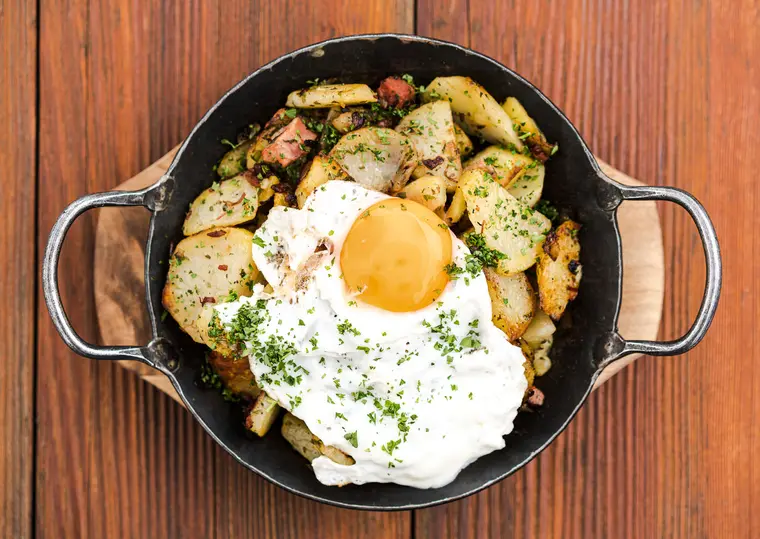 Pfanne mit Bratkartoffeln und Spiegelei auf Holztisch