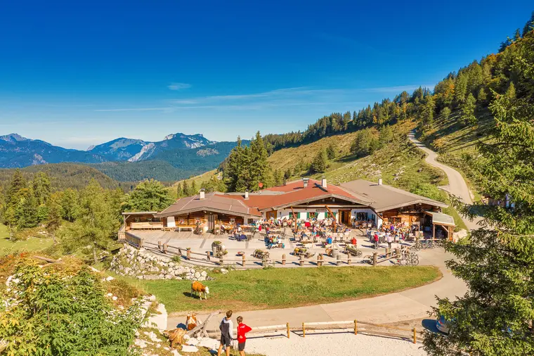 Almhütte mit Gästen vor Bergpanorama aus der Luft